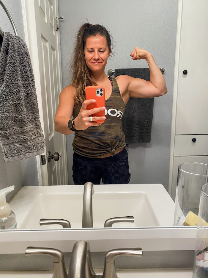 Woman in the mirror taking a selfie and flexing her bicep muscle.