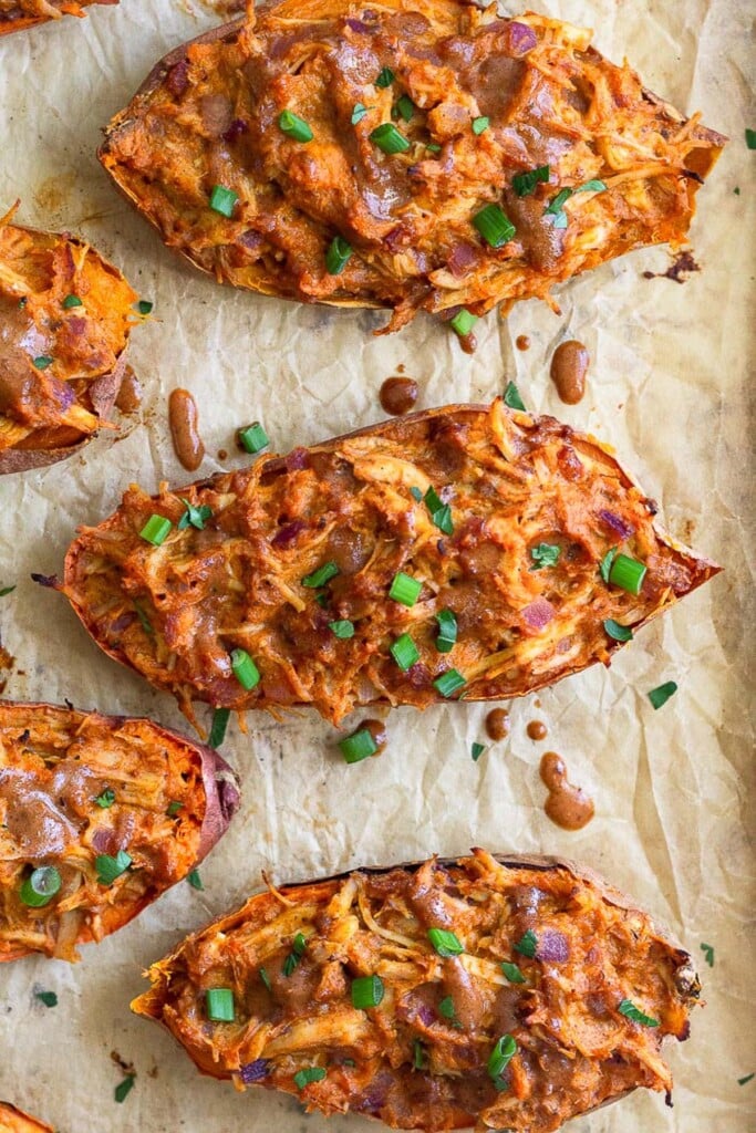 Overhead shot of twice-baked BBQ chicken sweet potatoes topped with diced green onions on a piece of parchment paper.