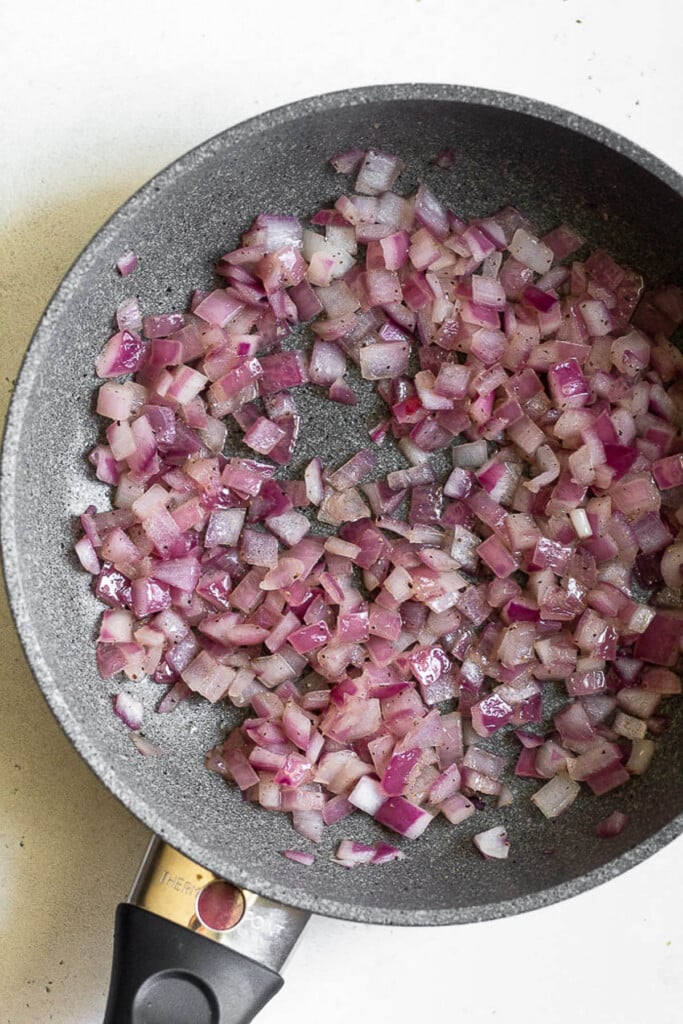 Small skillet filled with sautéed diced red onions.