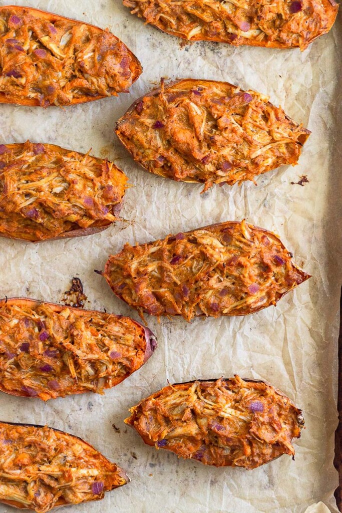 Chicken stuffed sweet potatoes on a baking sheet lined with parchment paper.