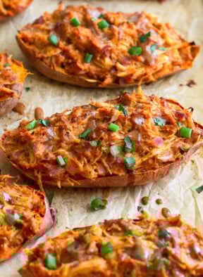 Twice baked BBQ chicken stuffed sweet potatoes on a baking sheet. They are garnished with more BBQ sauce and chopped green onions.