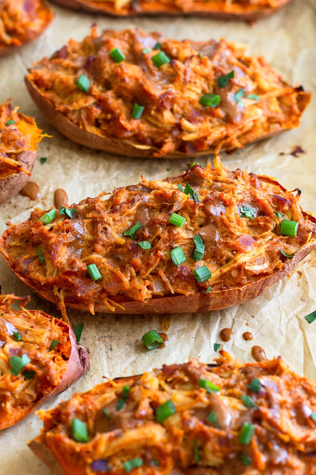 Twice baked BBQ chicken stuffed sweet potatoes on a baking sheet. They are garnished with more BBQ sauce and chopped green onions.