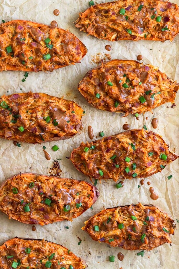 Overhead shot of BBQ stuffed sweet potatoes on a baking sheet. They are garnished with more BBQ sauce and diced green onions.
