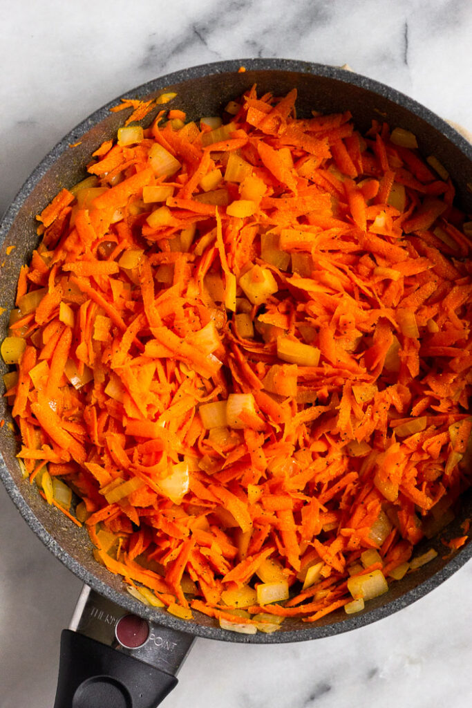 Small skillet filled with sautéed shredded carrots and onions.