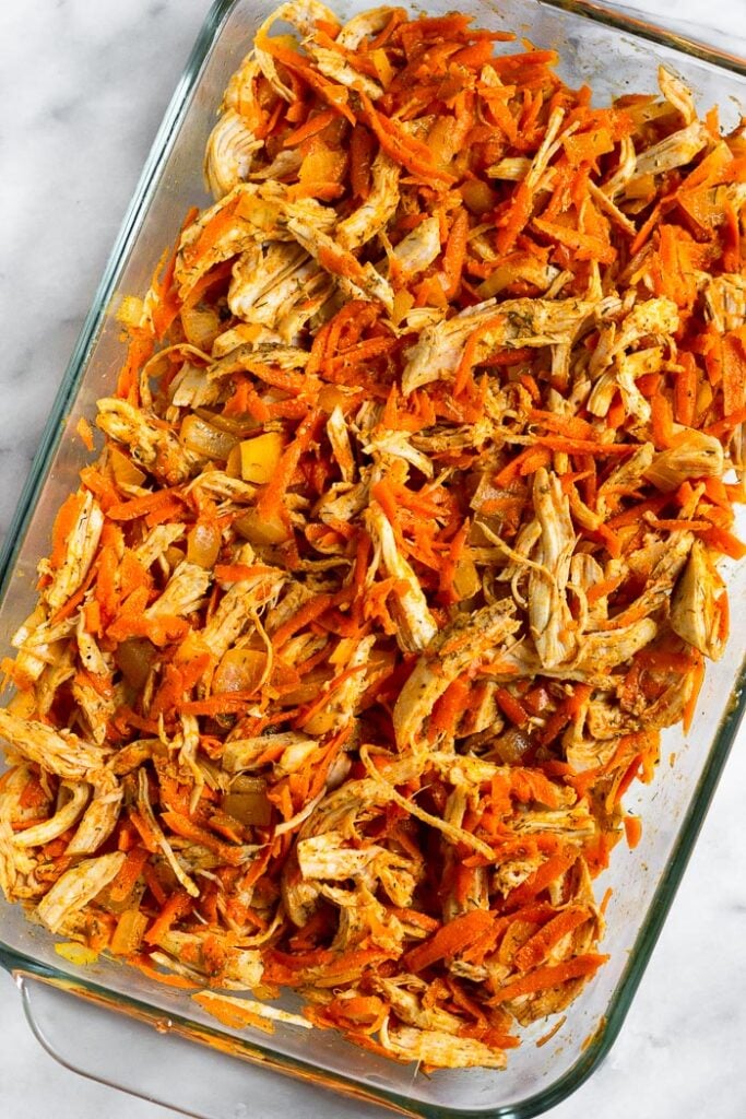 Glass baking dish filled with a mixture of shredded chicken, carrots, onions, spices, and buffalo sauce.