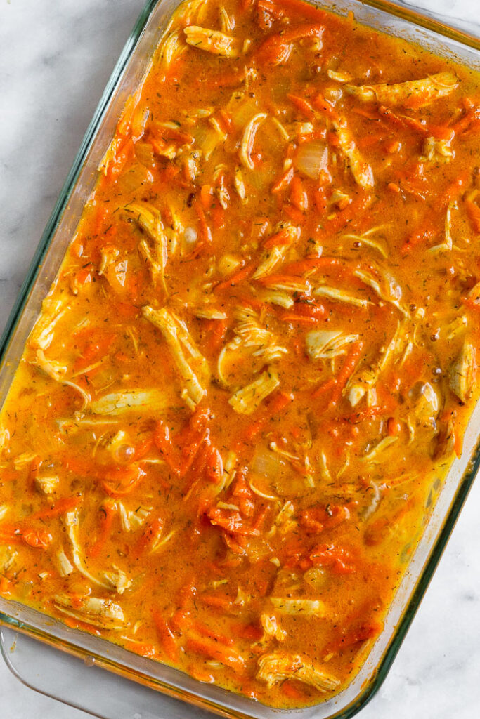 Casserole dish filled with a mix of shredded chicken, veggies, and whisked eggs.