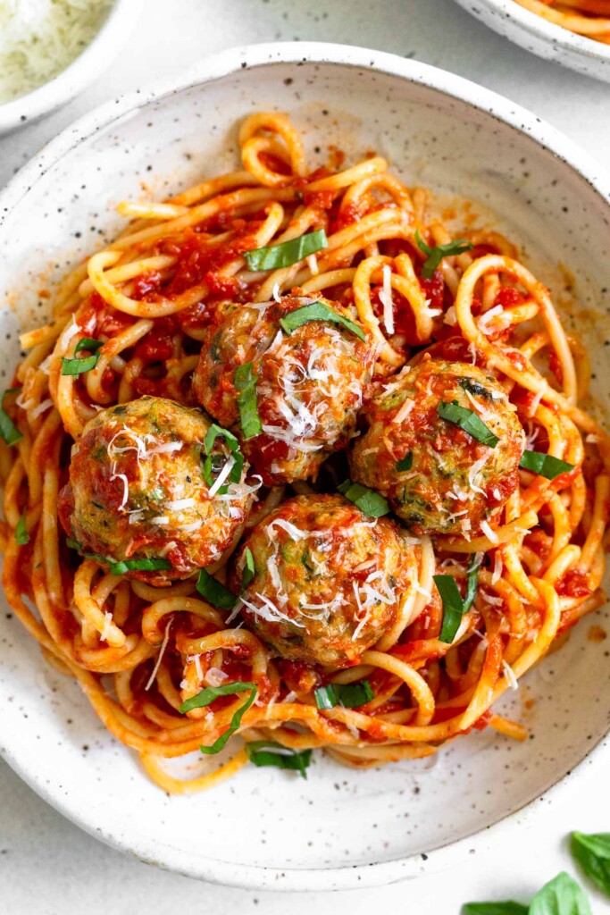Overhead shot of a bowl of pasta and chicken meatballs tossed in marinara sauce garnished with basil and parmesan cheese.