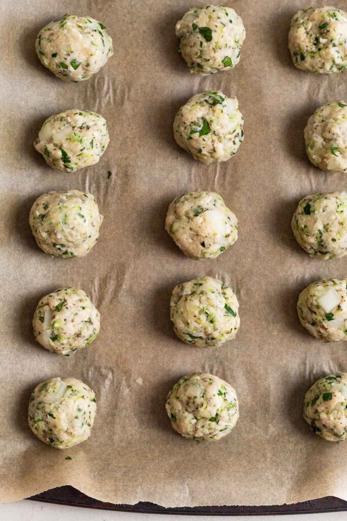 A baking sheet with raw chicken meatballs on it.