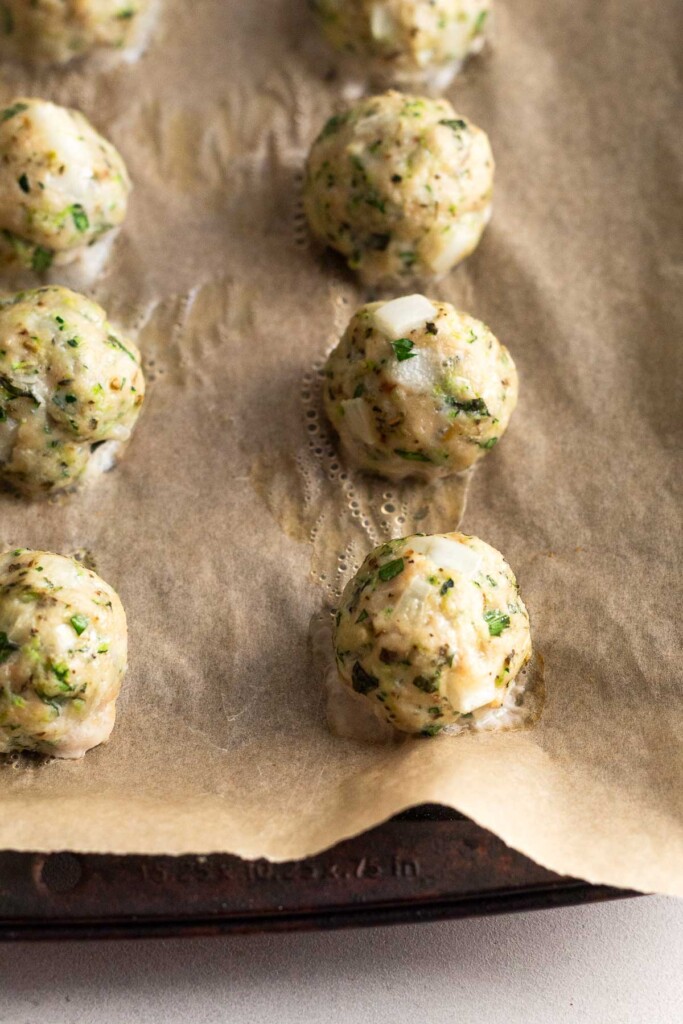 Baked chicken meatballs on a baking sheet lined with parchment paper. A little bit of juice is around each meatball.