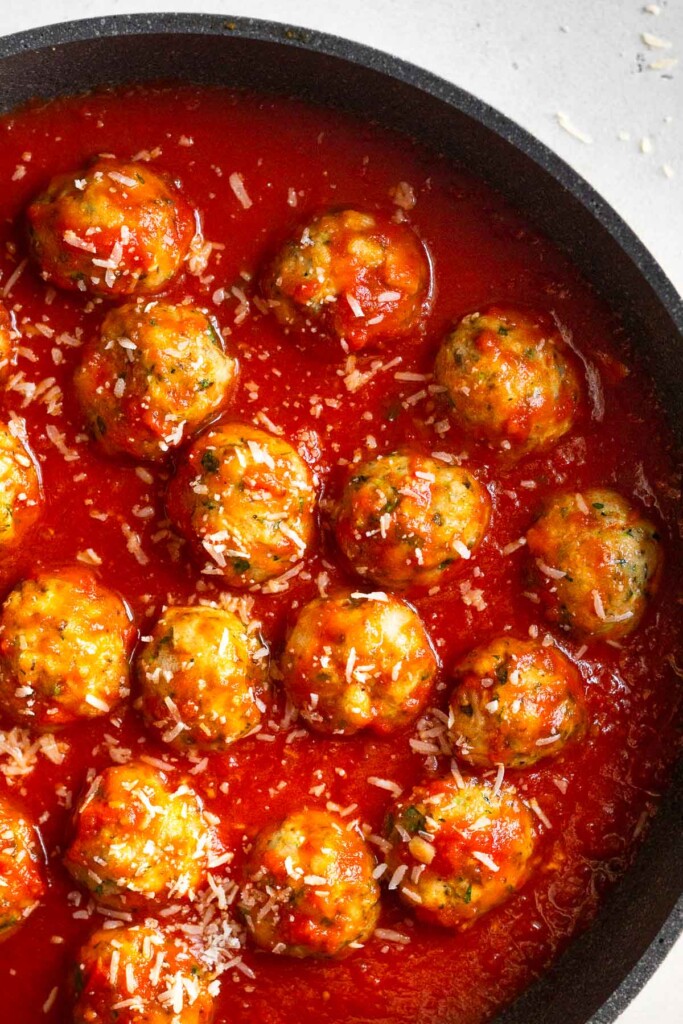 Overhead shot with a skillet filled with pasta sauce and zucchini chicken meatballs sprinkled with parmesan cheese in it.