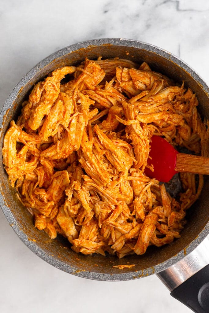 Saucepan of shredded buffalo chicken with a spatula in it.