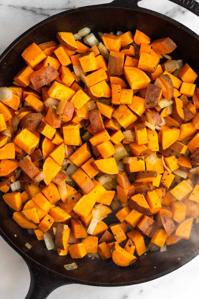 Large cast iron with sautéed diced sweet potatoes and onions in it.