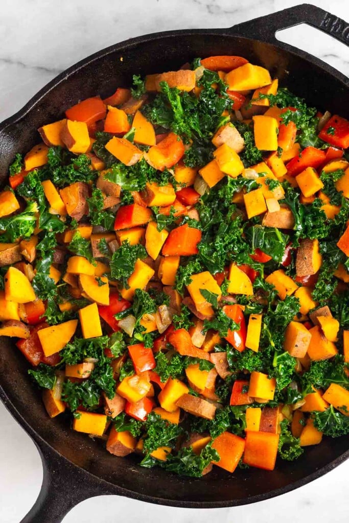 Large cast iron with sautéed sweet potatoes, onions, peppers, and kale in it.