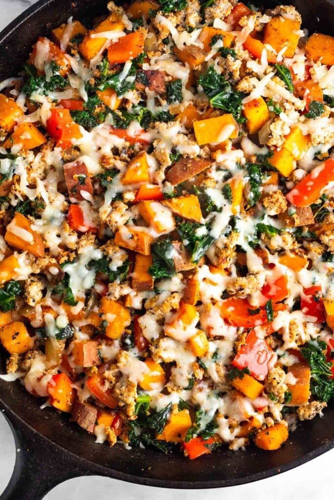 Turkey sweet potato skillet with veggies topped with melted cheese in a large cast iron.