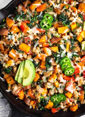 Ground turkey and sweet potato skillet with melted cheese in a large cast iron. It is topped with sliced avocado, jalapeño, and cilantro.
