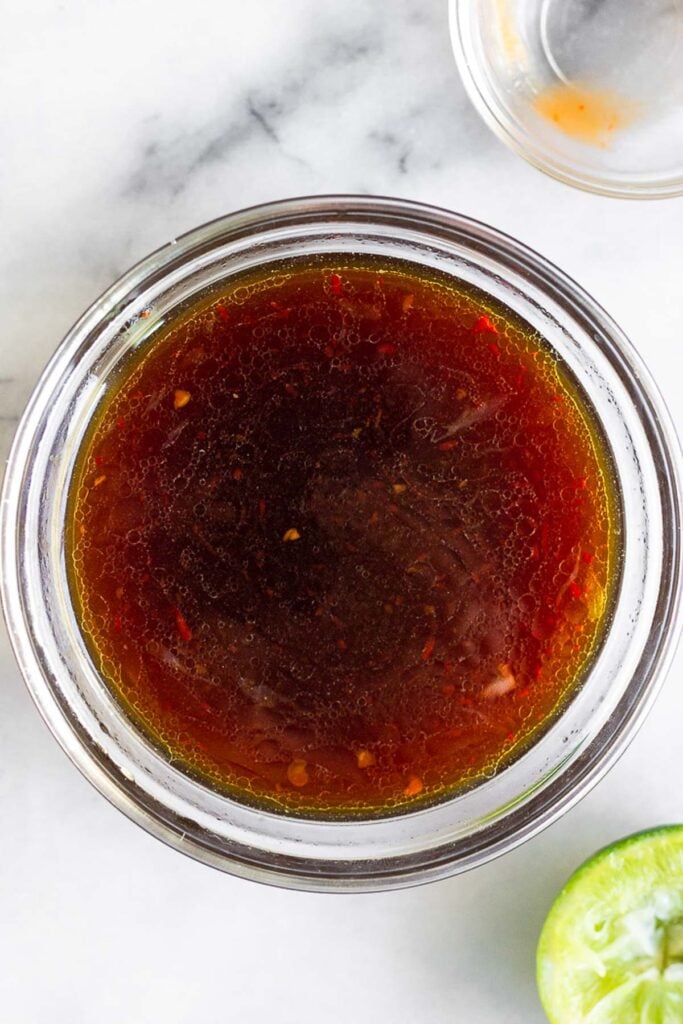 Small bowl of stir fry sauce. Next to it is half a lime and an empty bowl with a little sauce left in it.