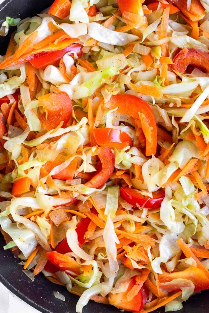 Close up of a large skillet filled with sautéed cabbage, peppers, and carrots.