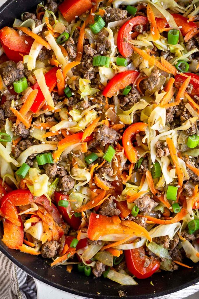 A close up of cabbage and ground beef stir fry in a cast iron topped with sesame seeds and green onions.