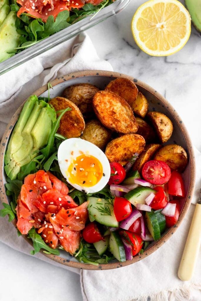 Healthy bowl recipe with potatoes, salad, smoked salmon, sliced avocado, and half a hard boiled egg in a bowl.