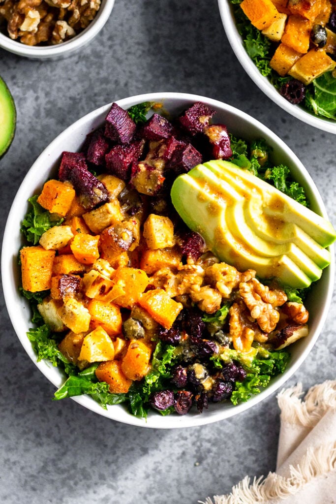Veggie power bowl with roasted butternut squash and beets, avocado, walnuts, and dried cranberries. It is topped with a little bit of dressing.