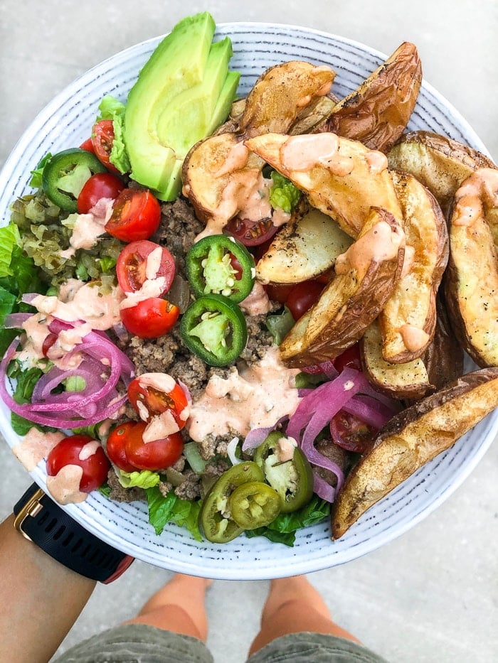 A plate of food being held up with veggies, ground beef, avocado, potatoes, and topped with a dressing.