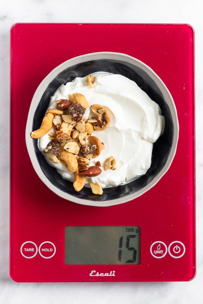 A bowl filled with yogurt and granola on a food scale.