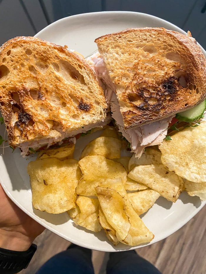 Plate of a sandwich and chips being heading by someone.