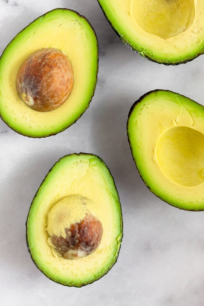 A few half of avocados on a white surface area.