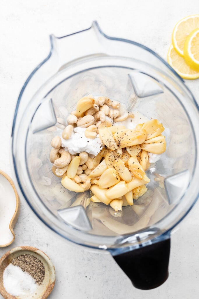Blender filled with coconut milk, cashews, lemon juice, and roasted garlic.