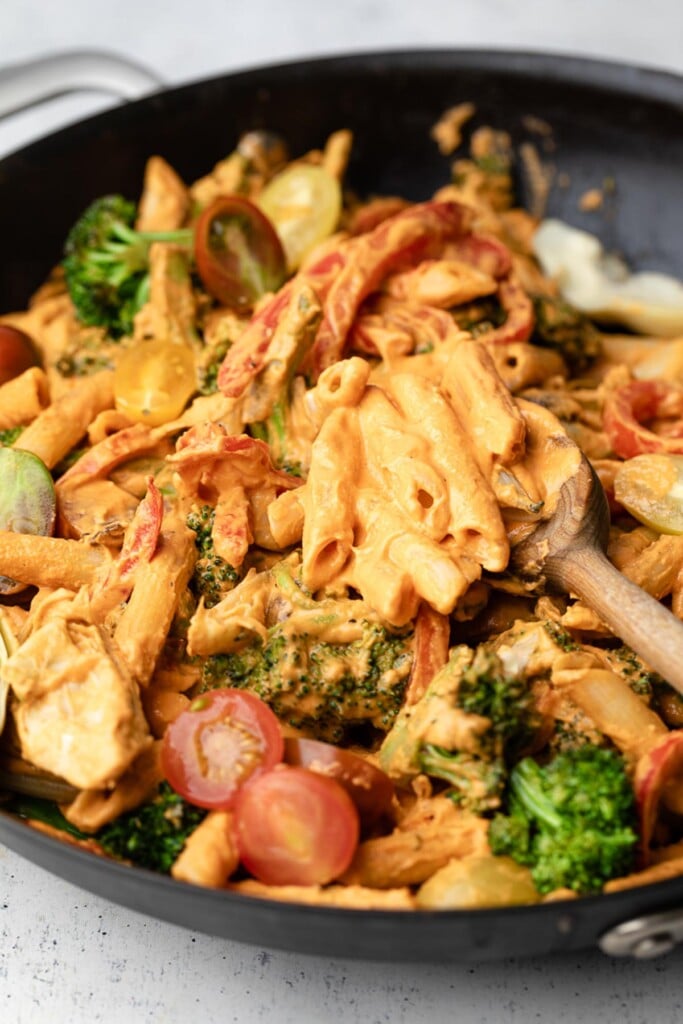 Large skillet with pasta and vegetables tossed in a creamy red sauce. A wooden spoon is also in the pan.