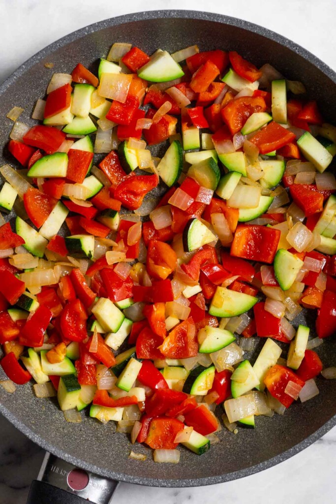 Skillet filled with sautéed onion, pepper, and zucchini.