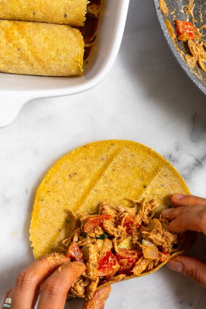 A corn tortilla topped with a shredded chicken and veggie mixture on about half of it about to be rolled up.