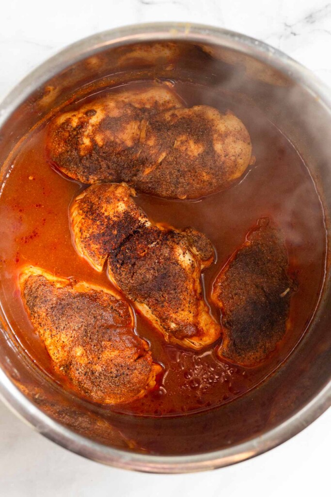 Large pot filled with barbecue sauce and cooked chicken breasts. Steam is coming off the food as it has just been cooked.