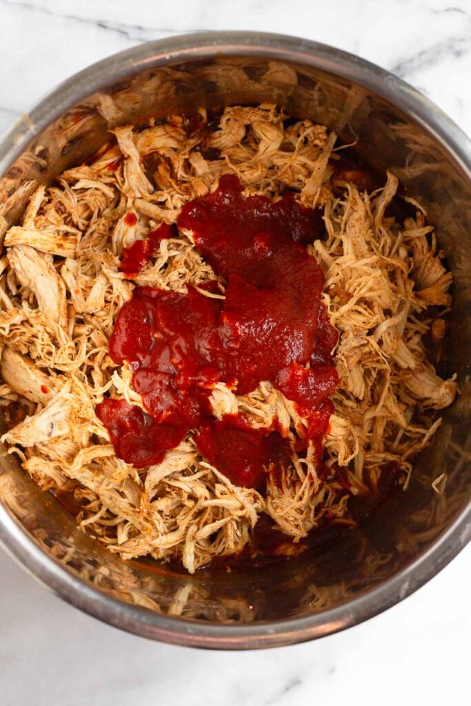 Pressure cooker filled with shredded chicken topped with barbecue sauce.