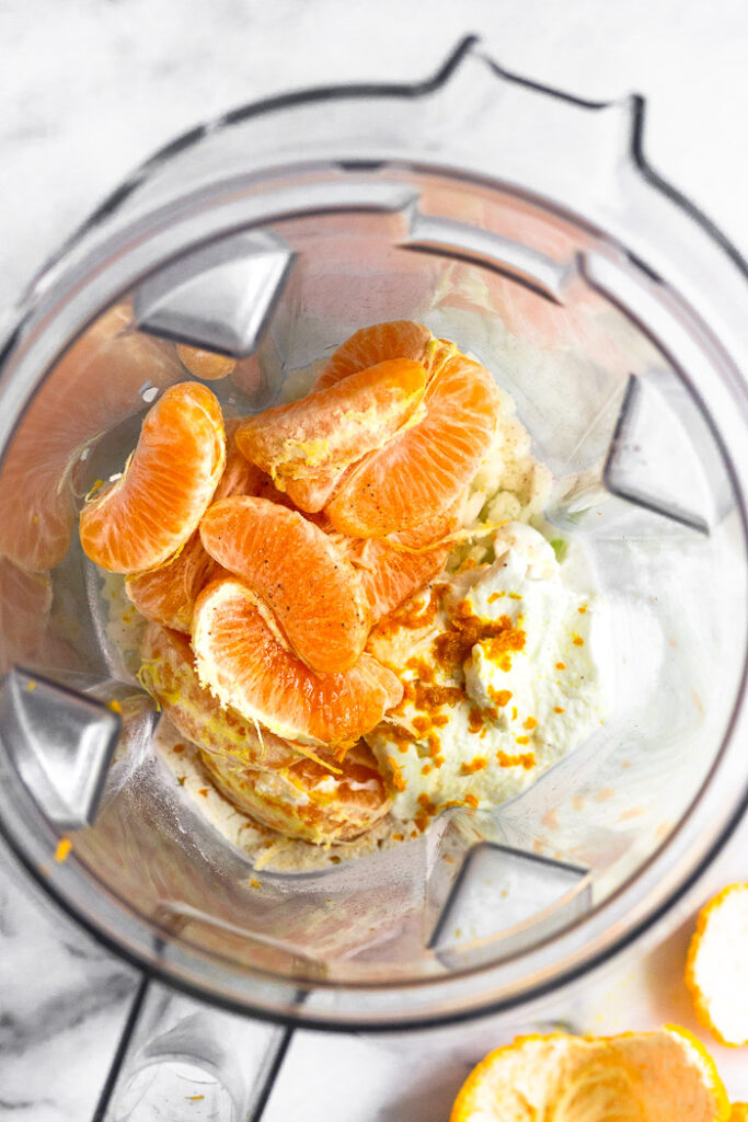 Blender filled with yogurt, oranges, orange zest, coconut milk, cauliflower rice, and vanilla extract.