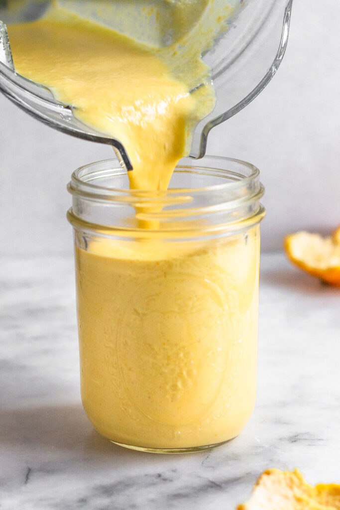 Blender pouring an orange smoothie into a glass. Behind the glass is orange peels.
