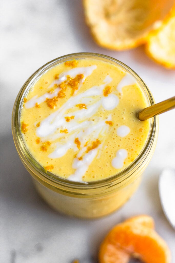 Overhead shot of an orange creamsicle protein smoothie topped with coconut milk and orange zest. Around it is some orange.