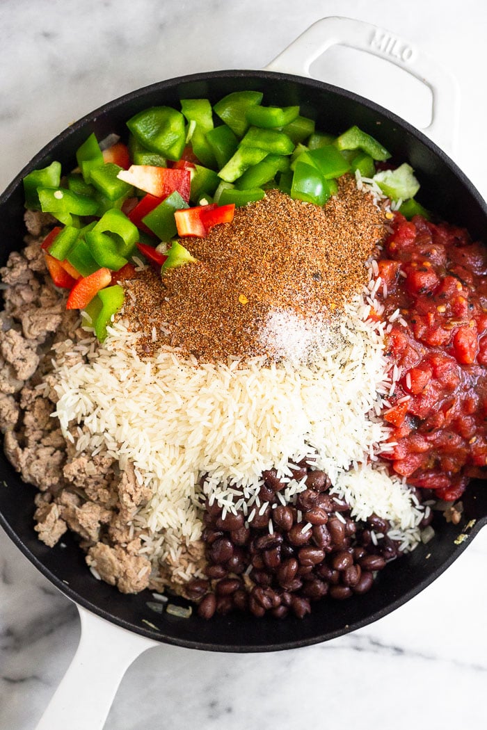 Large cast iron filled with sautéed ground turkey, diced bell peppers, canned diced tomatoes, black beans, uncooked white rice, and taco seasoning.