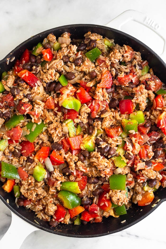 Overhead shot of a large cast iron filled with ground turkey, veggies, beans, diced tomatoes, and rice.