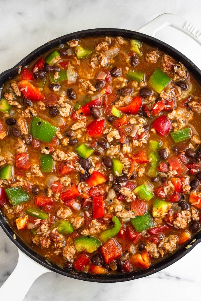Overhead shot of a large cast iron filled with ground turkey, veggies, beans, diced tomatoes, and rice with broth covering most of it.