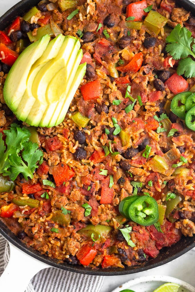 Turkey taco skillet with rice in a large cast iron topped with avocado, jalapeño, and cilantro.