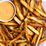 Air fryer French fries piled on a plate with a ramekin of special sauce.