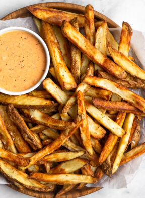 Air fryer French fries piled on a plate with a ramekin of special sauce.