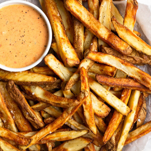 Air fryer French fries piled on a plate with a ramekin of special sauce.