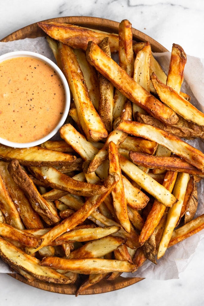 Air fryer French fries piled on a plate with a ramekin of special sauce.