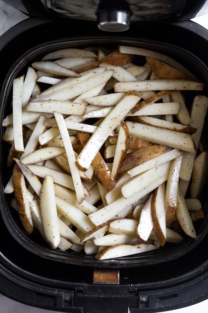 Homemade french fries in an air fryer basket before they are cooked.