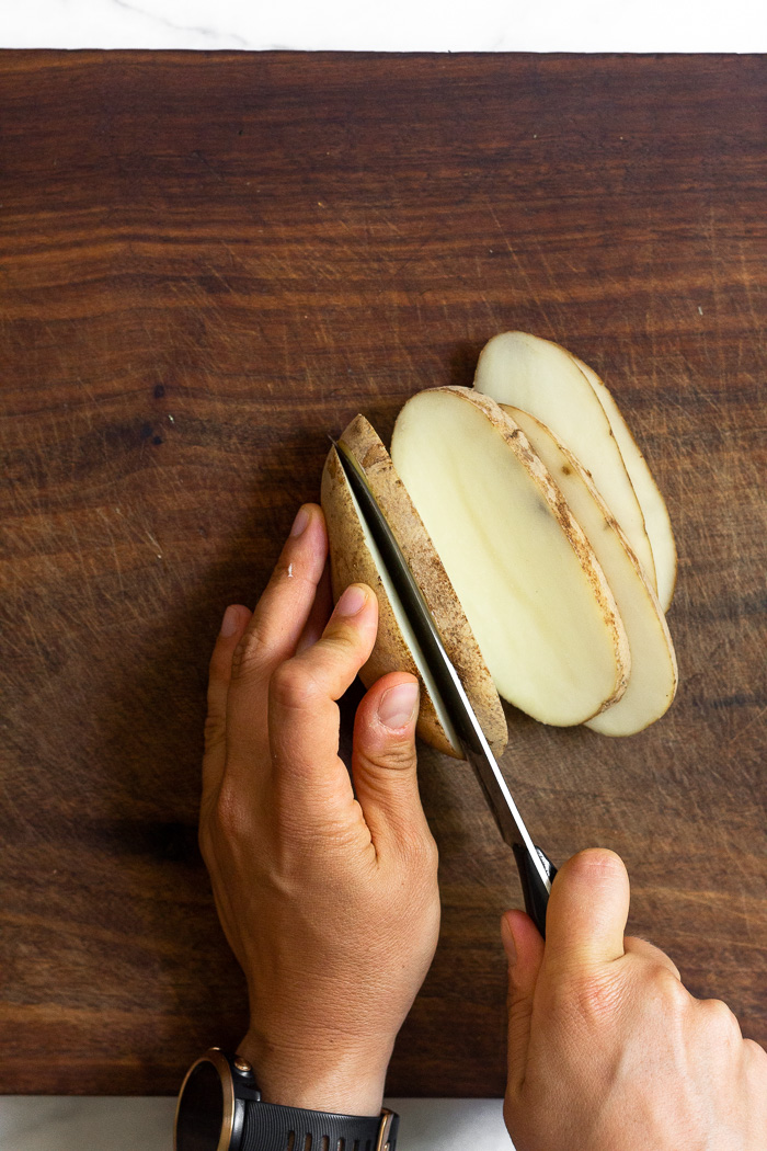 Overhead shot of someone cutting a potato lengthwise into 1/2 inch pieces.