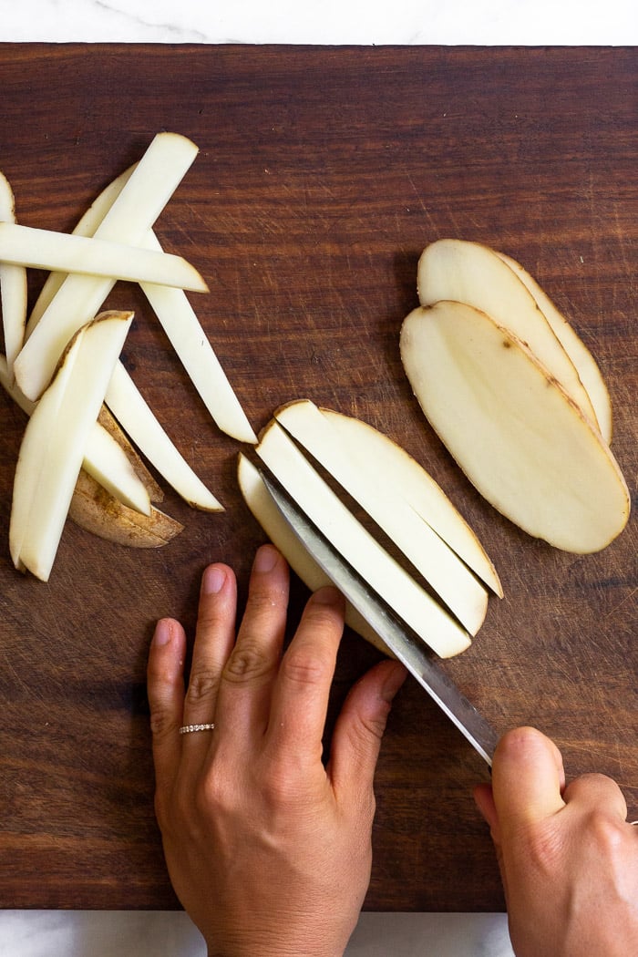 Overhead shot of someone cutting homemade french fries on a cutting board.