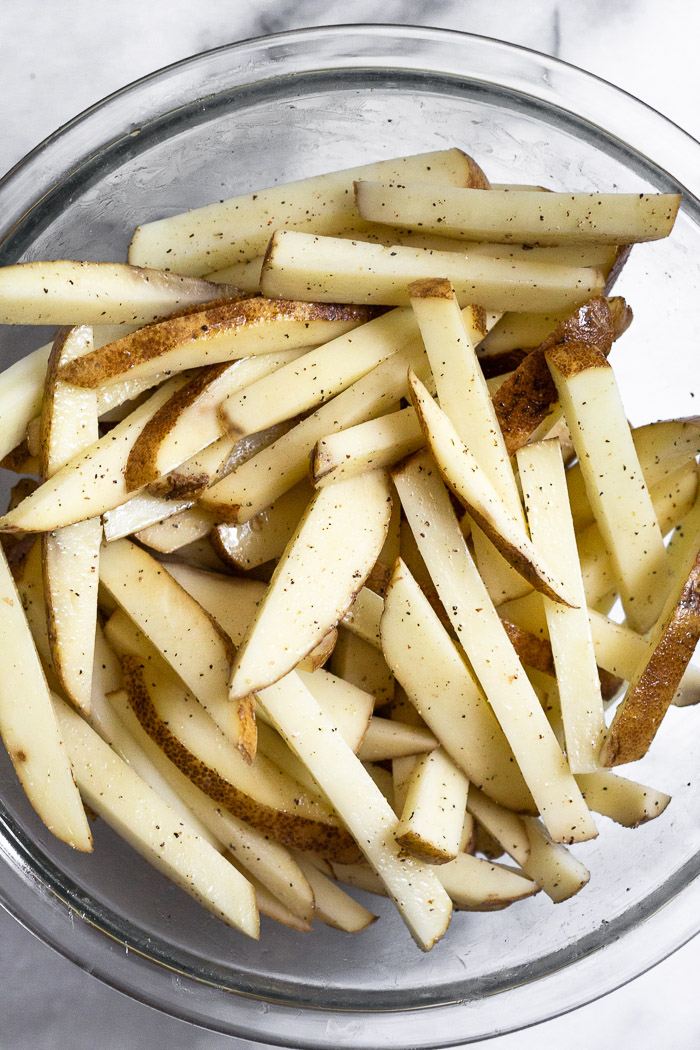 Overhead shot of raw potatoes cut into french fries in a large bowl.