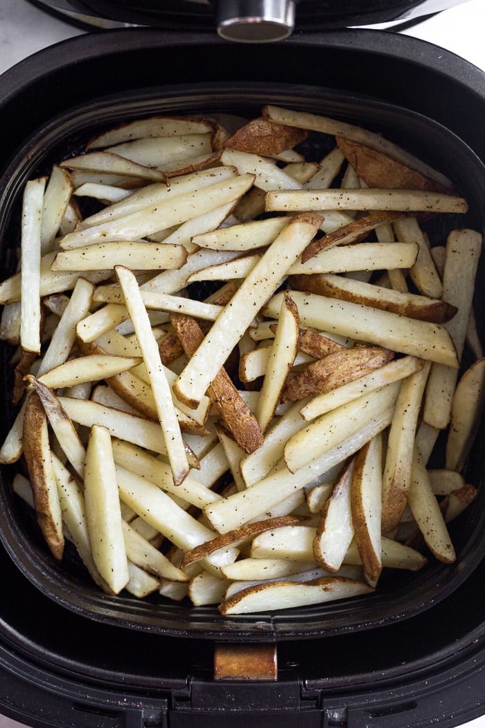 Par-cooked french fries in an air fryer basket.